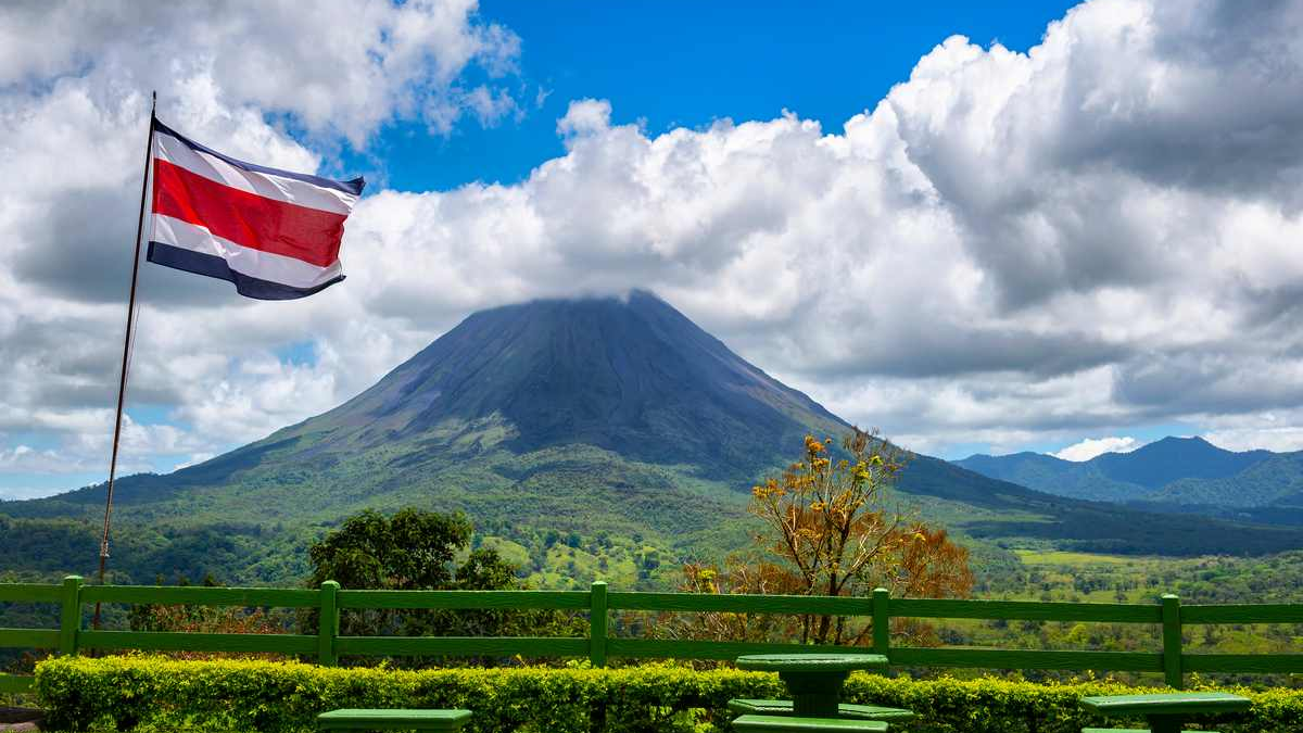 Paisagem natural ao fundo, bancos de madeira e uma bandeira da costa rica